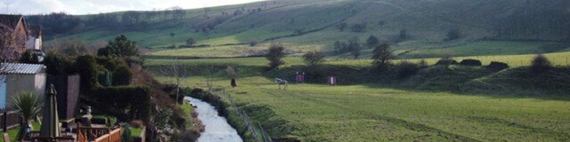 River Beal, Newhey Looking south from the bridge at the end of Bentgate Street. The rear gardens of houses on Whitebeam Close have been extended onto the river bank. The houses on the east bank are in Rochdale whilst the grazing land on the west bank is in Oldham. The ridge on the skyline carries the Rochdale Way, the Oldham Way and the Crompton Circuit footpaths.