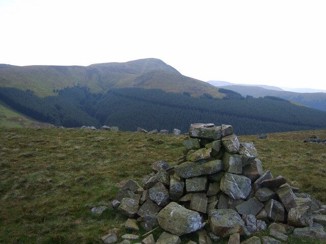 A stone cairn on a grassy hill with a forested valley in the background.