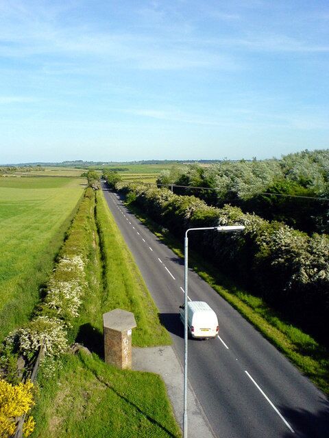 A rural road with a white van, surrounded by green fields and hedgerows.