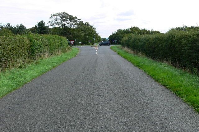 A rural road with a speed limit sign, a van, and hedges on both sides.