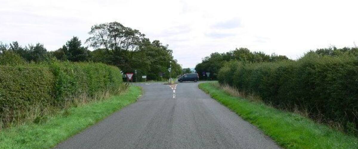 A rural road with a speed limit sign, a van, and hedges on both sides.
