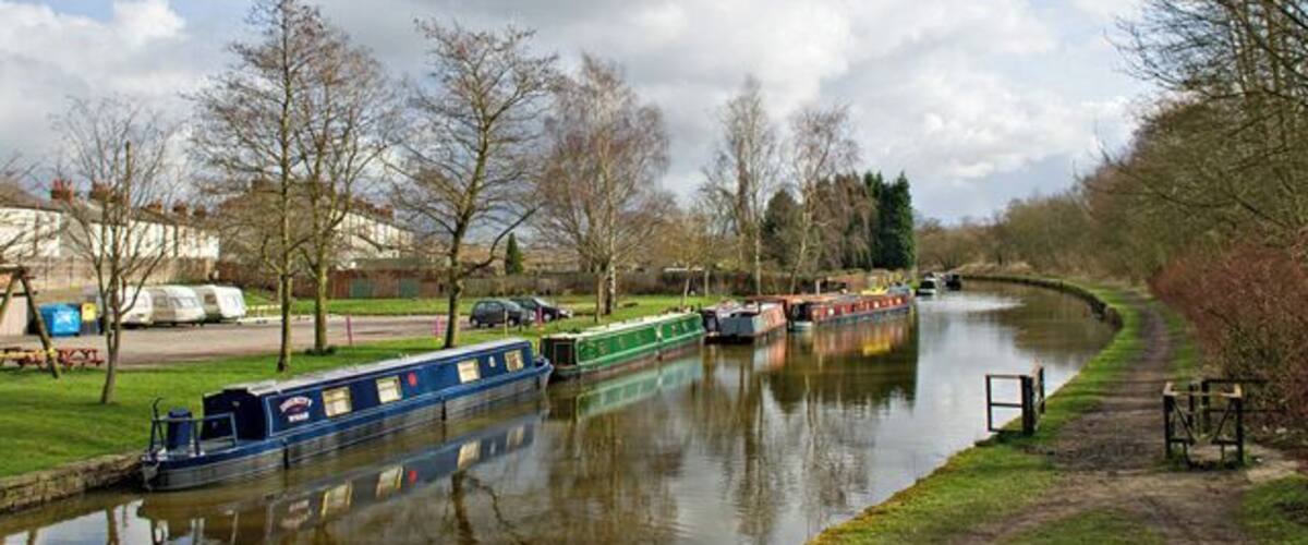A canal with boats, trees, and a grassy bank.