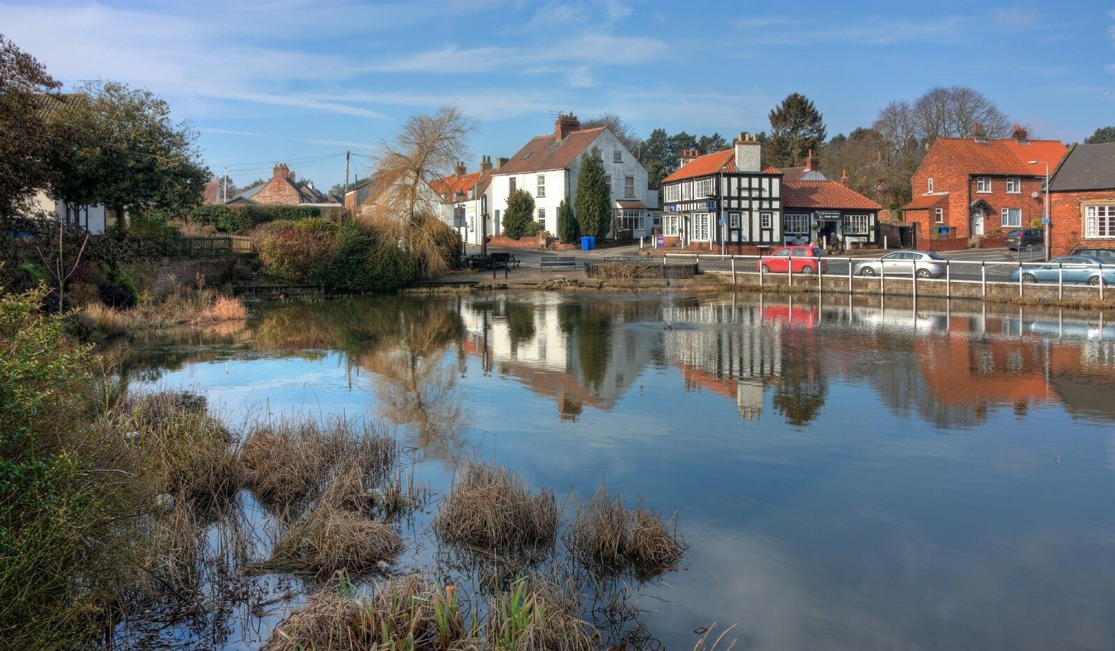 A calm river reflecting buildings and trees, with a mix of traditional and modern architecture.