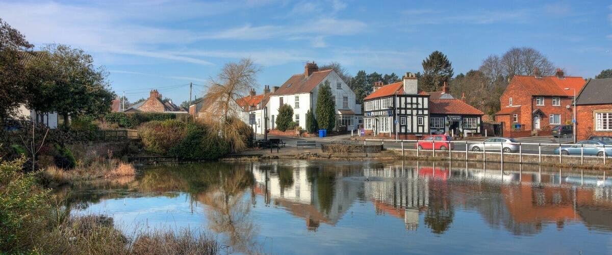 A calm river reflecting buildings and trees, with a mix of traditional and modern architecture.