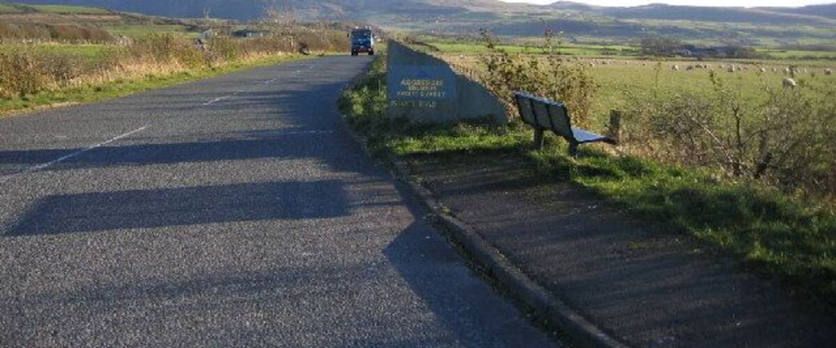 A rural road with a bench and a signboard.