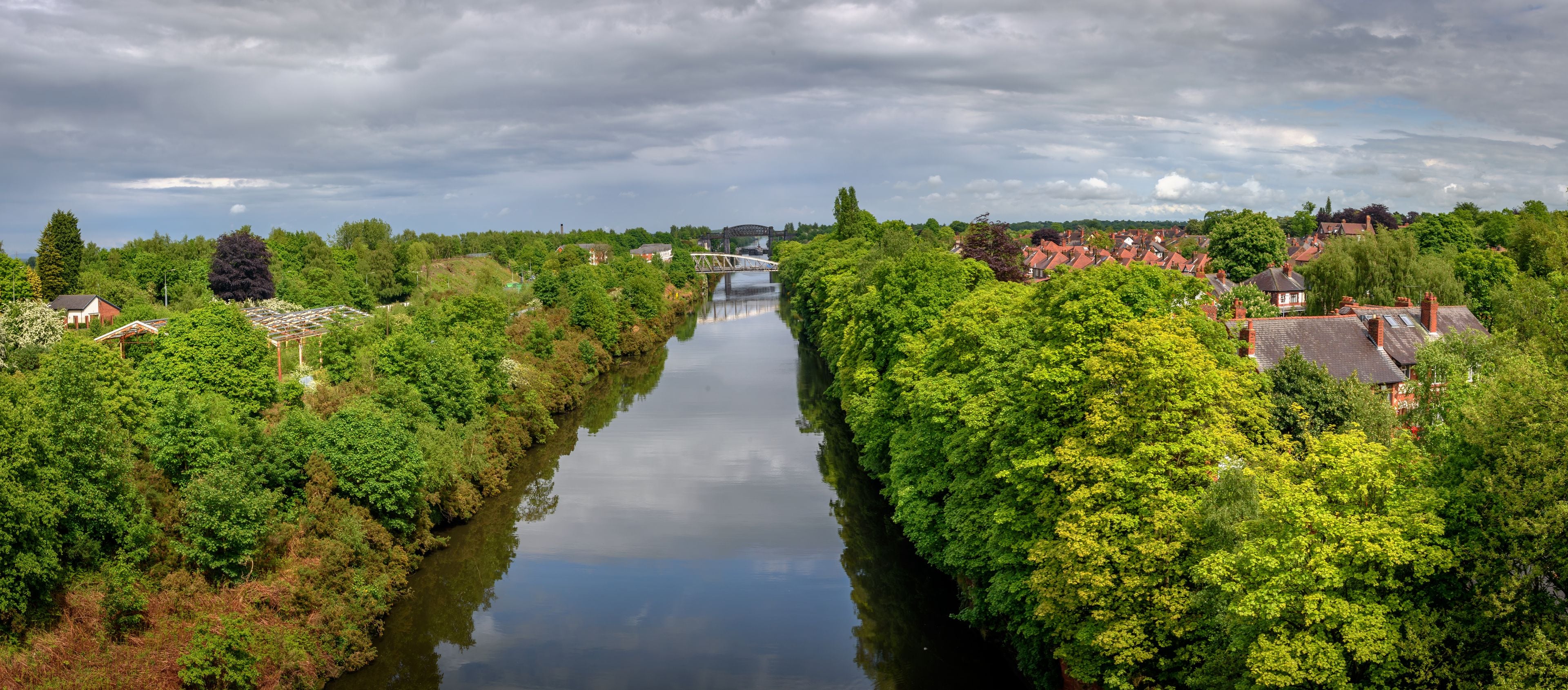 Ein Fluss, der von üppigem Grün und Häusern mit roten Dächern gesäumt wird.