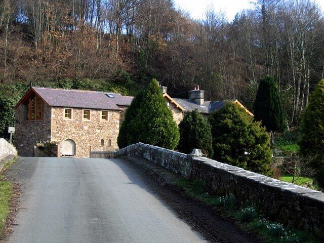 A stone house with a red roof, a stone wall, and a paved road.