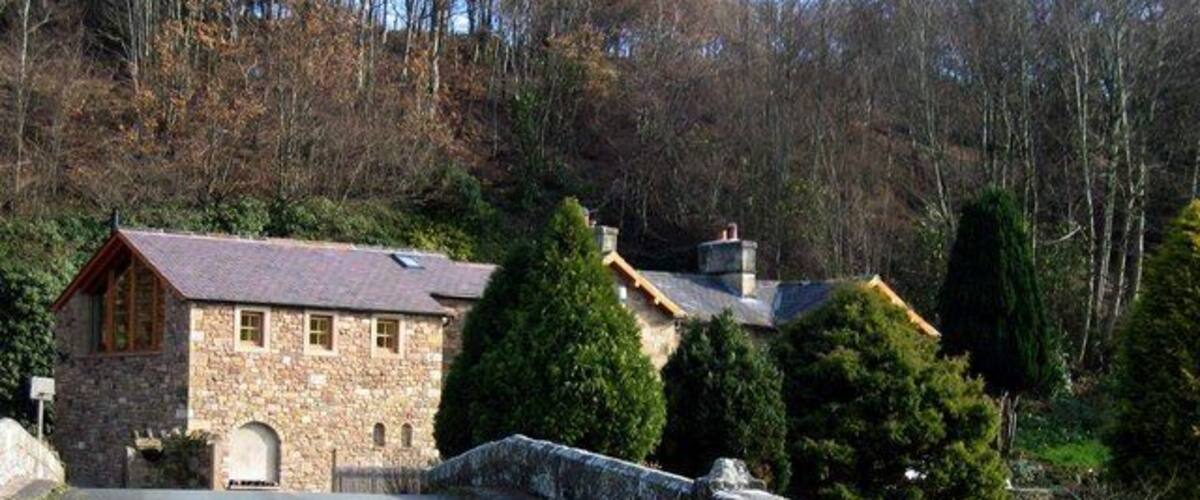 A stone house with a red roof, a stone wall, and a paved road.