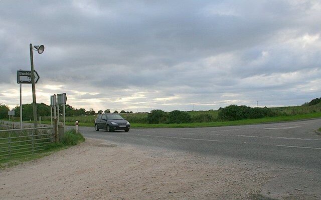 A rural road with a car, a directional sign, and a guardrail.