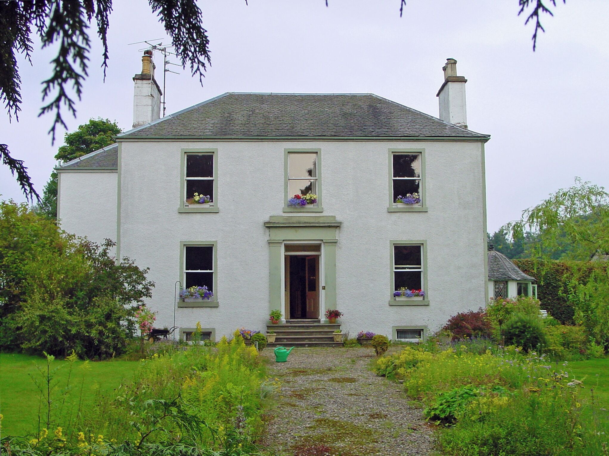 A white house with green shutters, a front door, and flower boxes on the windows.