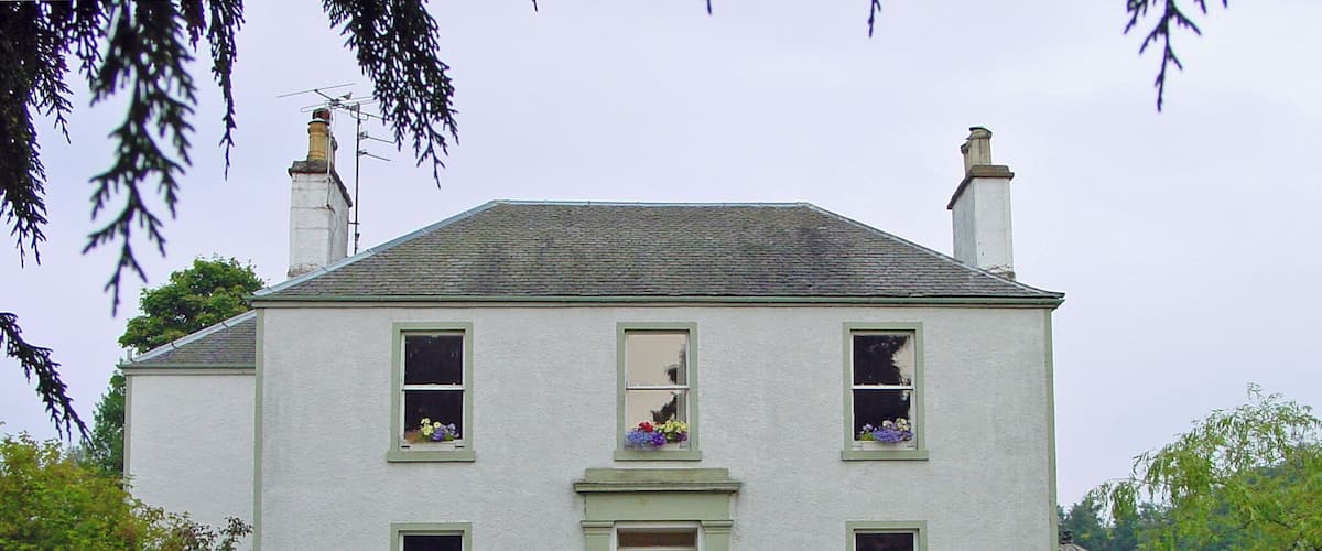 A white house with green shutters, a front door, and flower boxes on the windows.