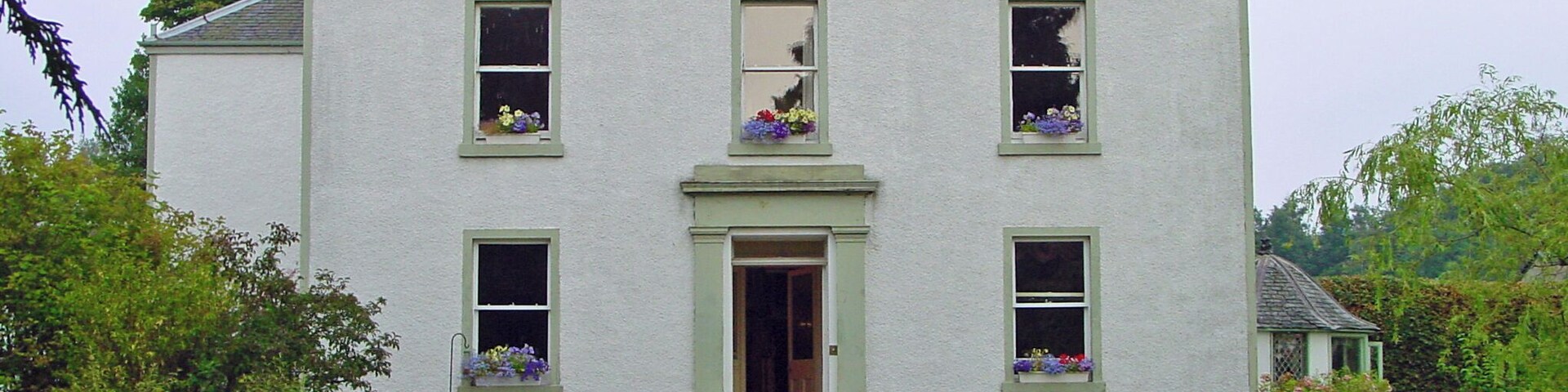 A white house with green shutters, a front door, and flower boxes on the windows.