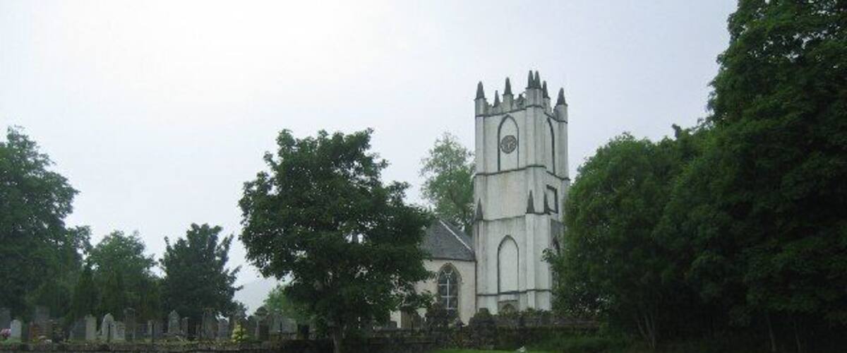 A church with a clock tower, surrounded by trees and a stone wall.