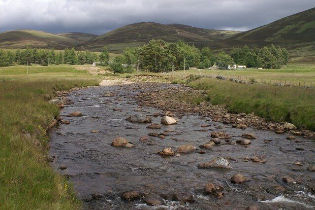 A river with rocks, grassy banks, and hills in the background.