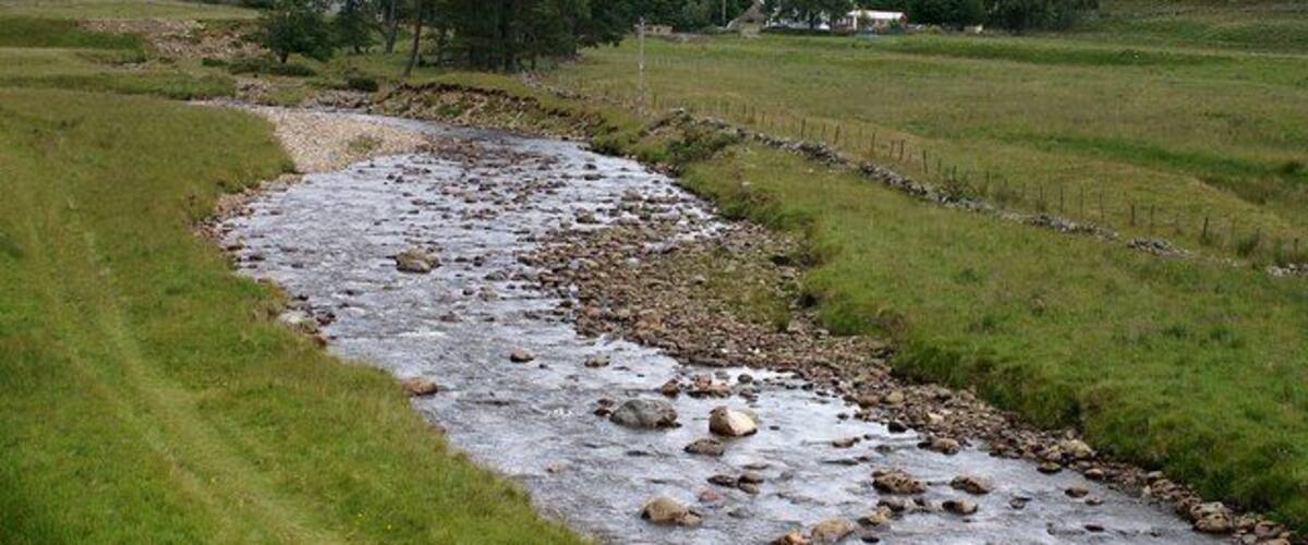 A river flowing through a grassy valley with hills in the background.
