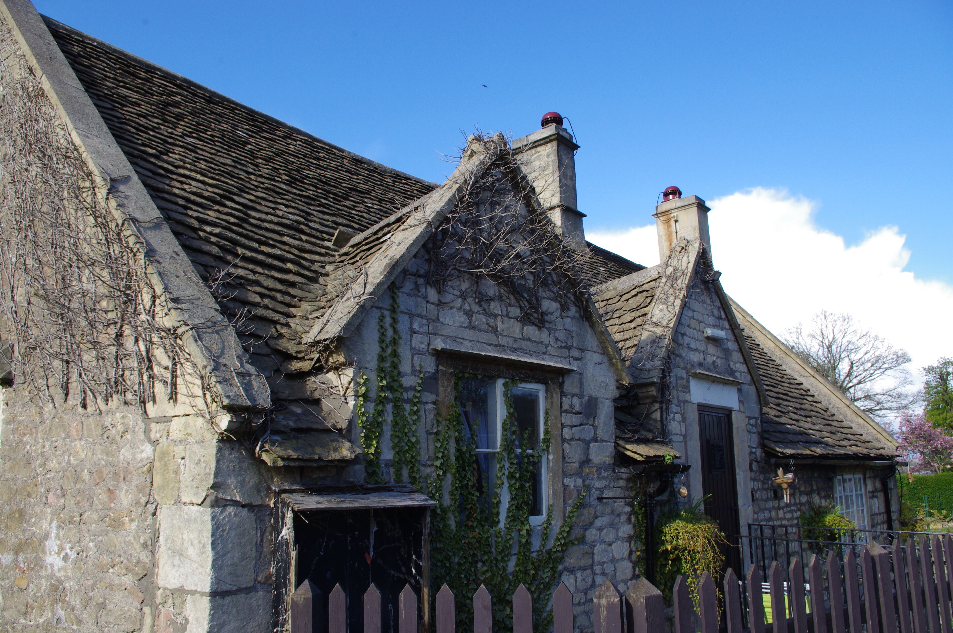 A stone house with ivy, a picket fence, and a clear blue sky.