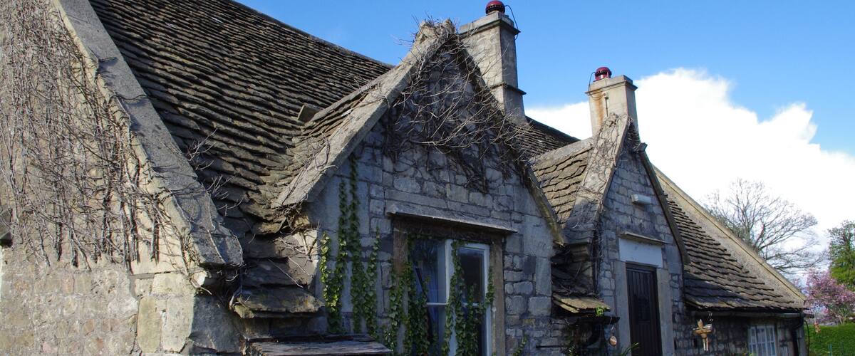 A stone house with ivy, a picket fence, and a clear blue sky.