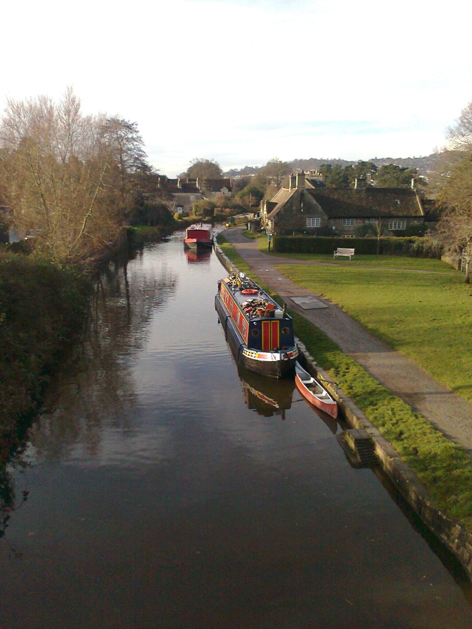 A narrow canal with boats, a grassy bank, and houses in the background.
