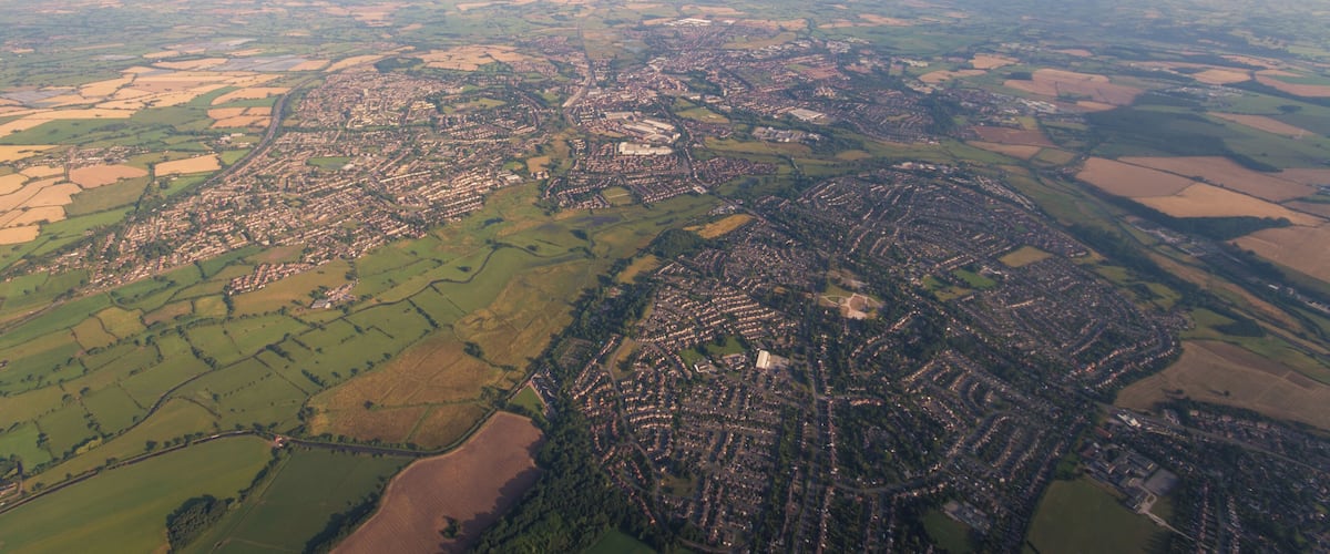 An aerial view of a town with a river, green fields, and a large open area.