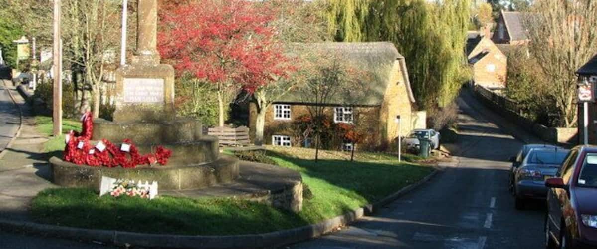 A village street with a stone monument, a house, and a flag.