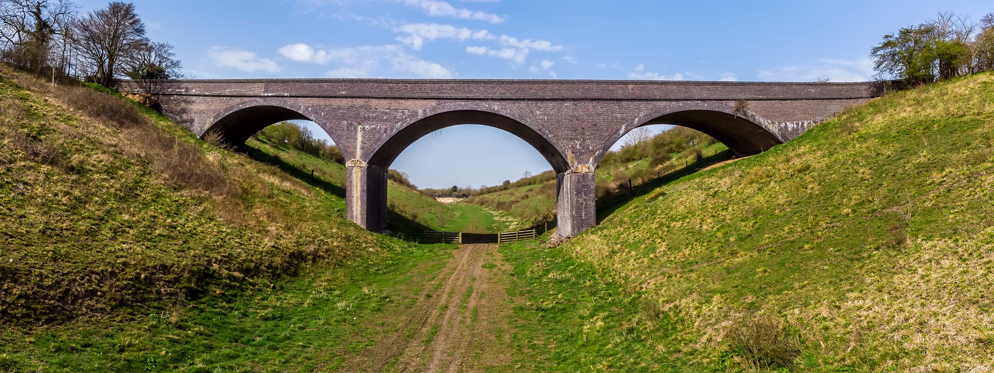 A stone viaduct with three arches over a grassy valley.
