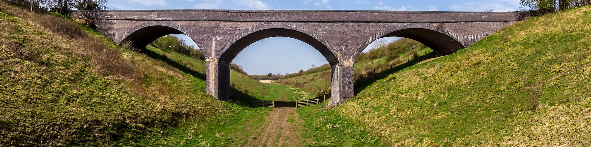 Um viaduto de pedra com três arcos sobre um vale gramado.