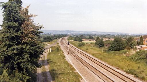 Site of Churchdown station, 1986. View NE, towards Cheltenham etc.: ex-GW & Midland Joint Gloucester etc. - Cheltenham etc. main line. This important line had been quadrupled for War traffic in 1942, but reverted to double-track in 1967. Churchdown station was closed from 2/11/64. (See also several other scenes, SO8820 : Cheltenham - Paddington express passing Churchdown station etc.).