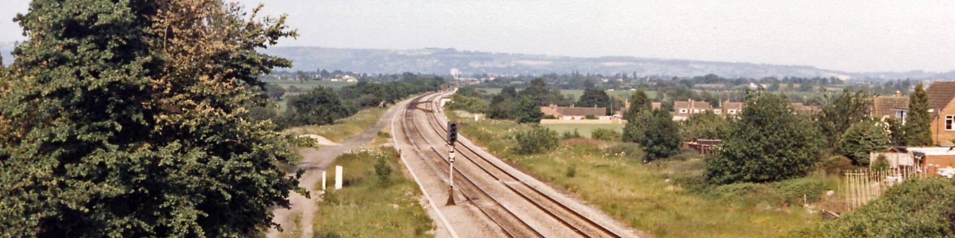 Site of Churchdown station, 1986. View NE, towards Cheltenham etc.: ex-GW & Midland Joint Gloucester etc. - Cheltenham etc. main line. This important line had been quadrupled for War traffic in 1942, but reverted to double-track in 1967. Churchdown station was closed from 2/11/64. (See also several other scenes, SO8820 : Cheltenham - Paddington express passing Churchdown station etc.).