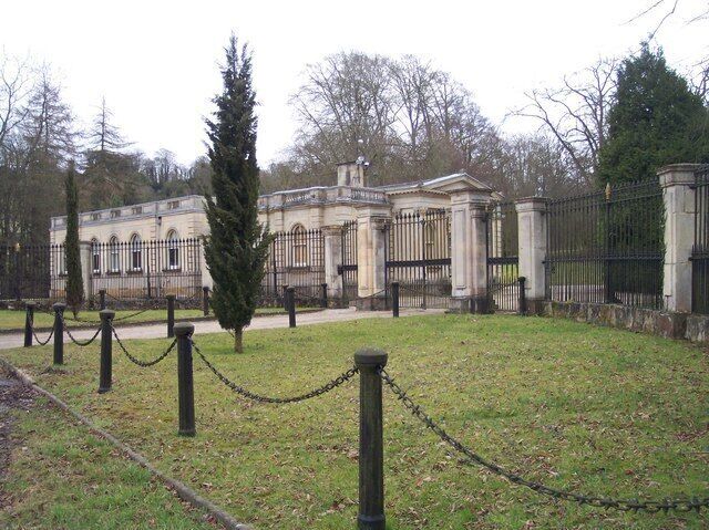 A classical building with columns, a chain-link fence, and a tall evergreen tree.