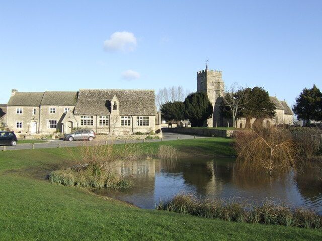 A historic stone building with a tower, a pond, and a grassy field.