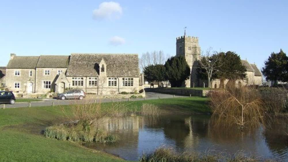 A historic stone building with a tower, a pond, and a grassy field.