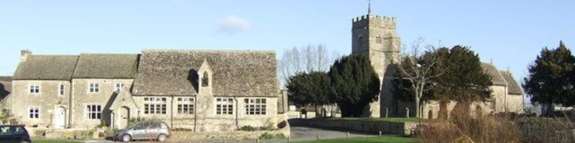 A historic stone building with a tower, a pond, and a grassy field.