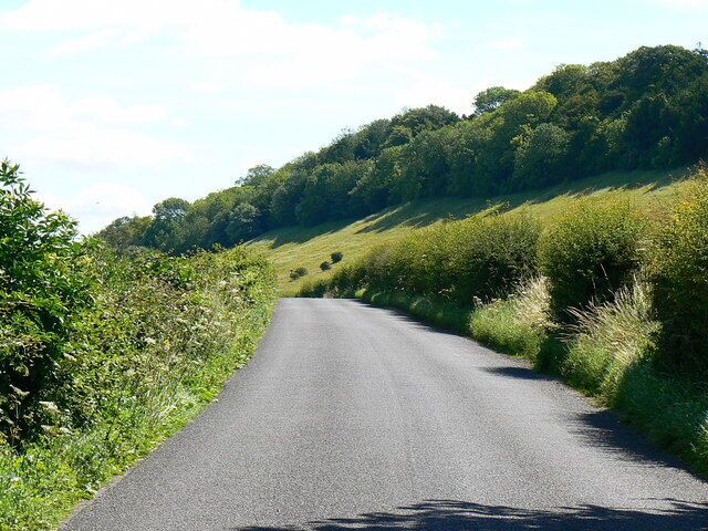 Road to West Dean This minor road runs at the foot of a fairly steep escarpment visible on the right. There was very little traffic on the road on this occasion.