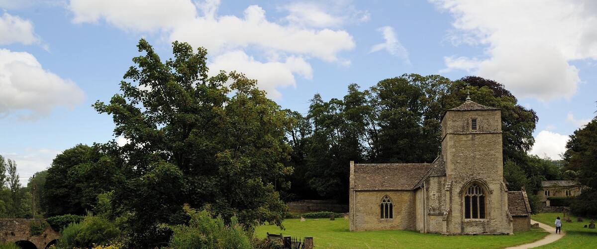A stone church with a tower, surrounded by lush greenery and a river.