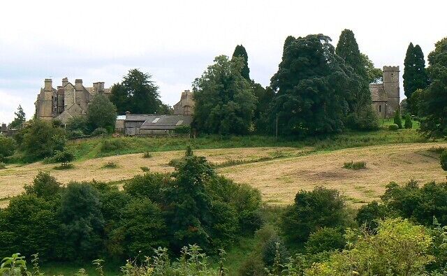 A historic building with a large tower, surrounded by trees and open fields.