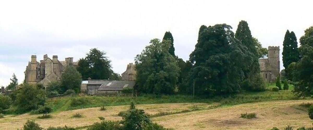 A historic building with a large tower, surrounded by trees and open fields.