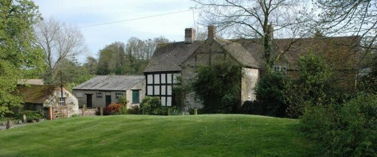 A rural landscape with a grassy hill, a traditional stone house, and a road.