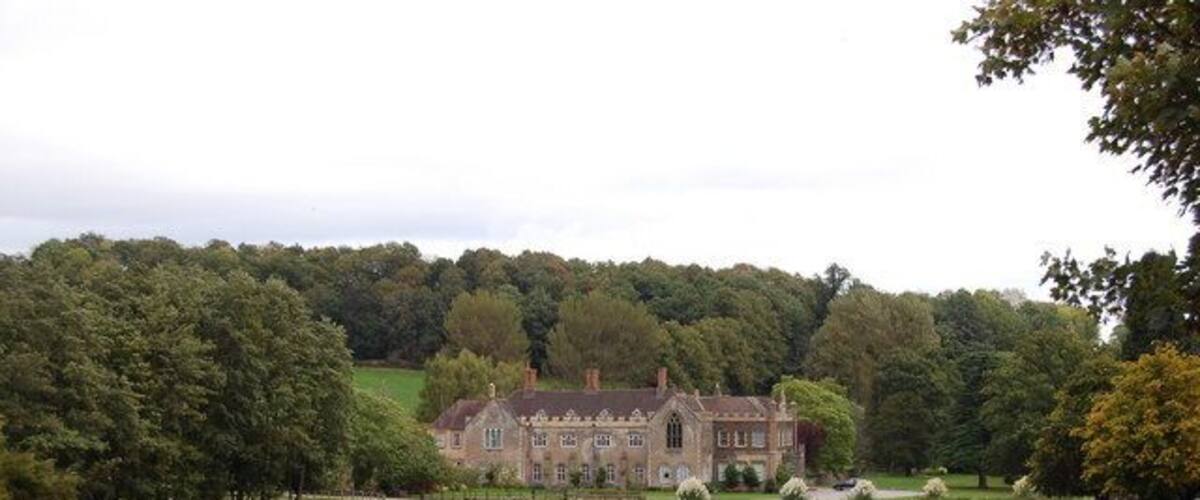 A large estate with a prominent building, surrounded by a fenced field and dense trees.