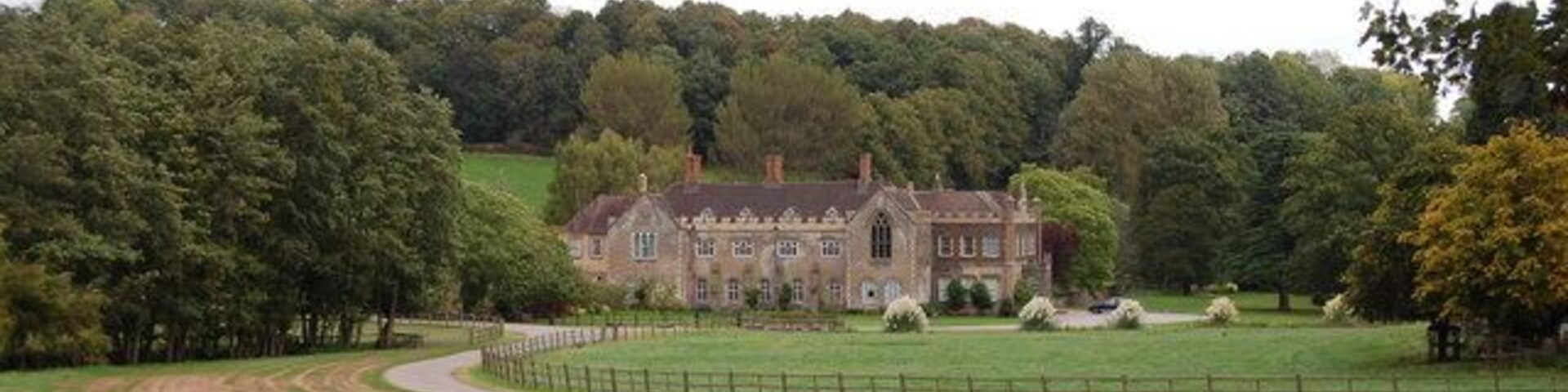 A large estate with a prominent building, surrounded by a fenced field and dense trees.