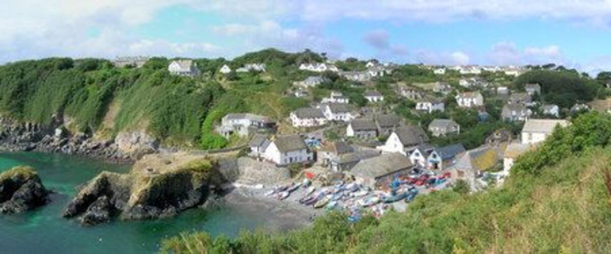 A coastal village with houses on a hillside, a rocky shoreline, and boats in the water.