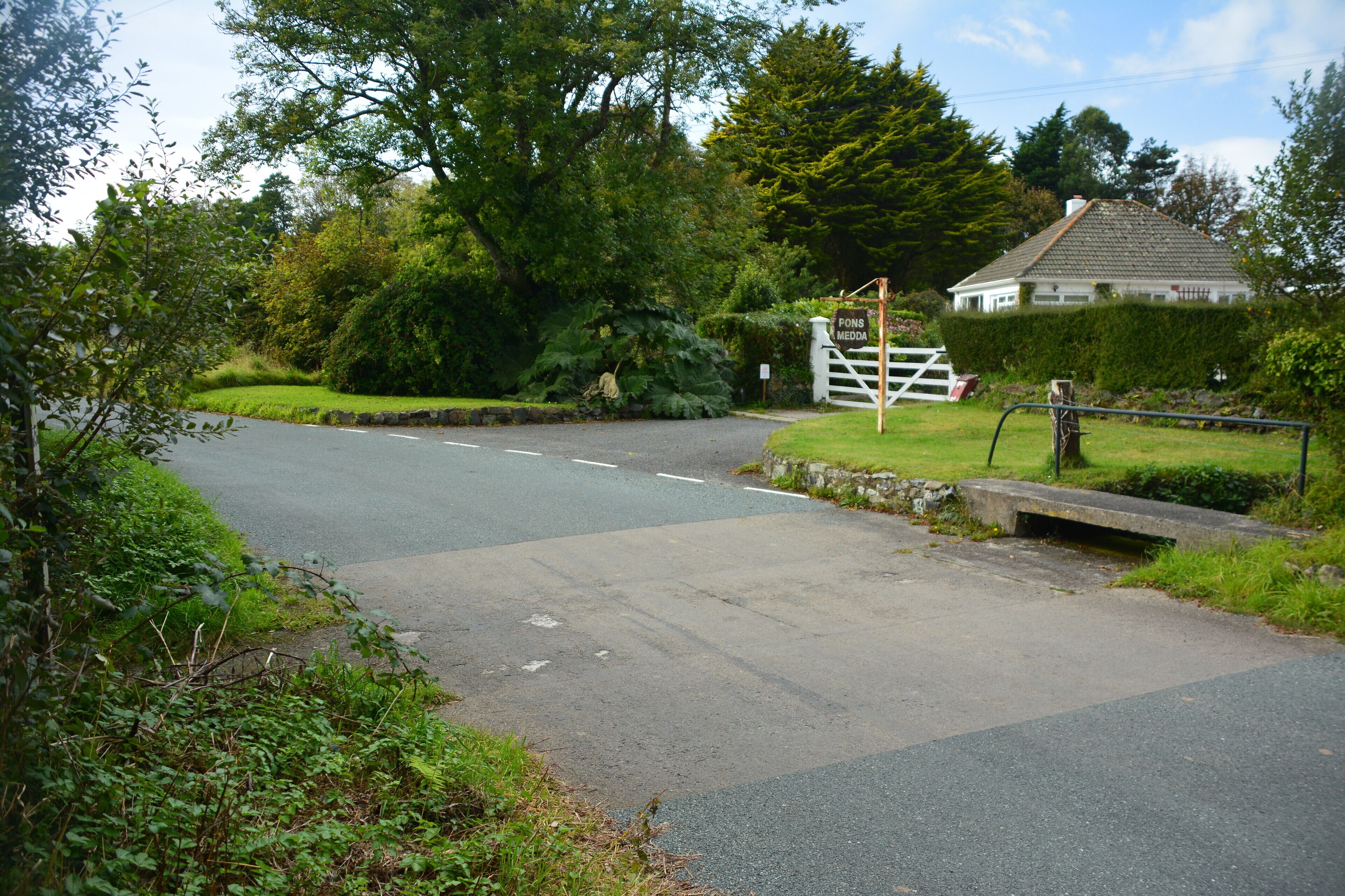 A rural road with a white gate and a house in the background.