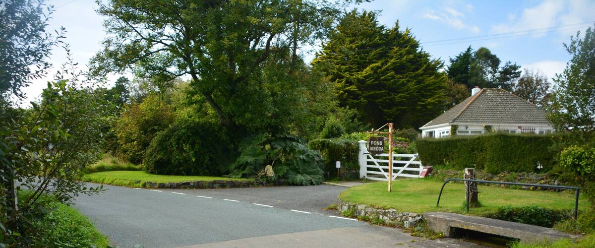 A rural road with a white gate and a house in the background.