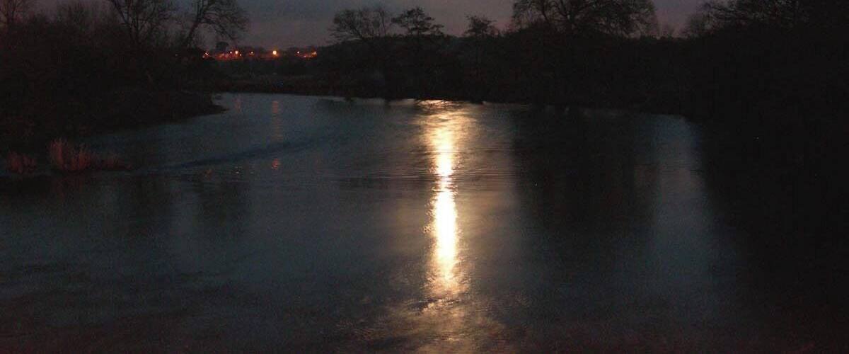 A river reflecting the moonlight with trees on the banks.