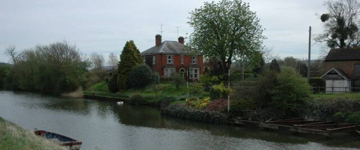 A calm river with a house and a boat on the left bank.