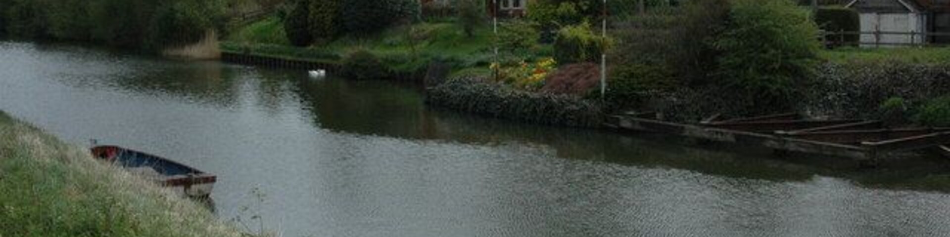 A calm river with a house and a boat on the left bank.