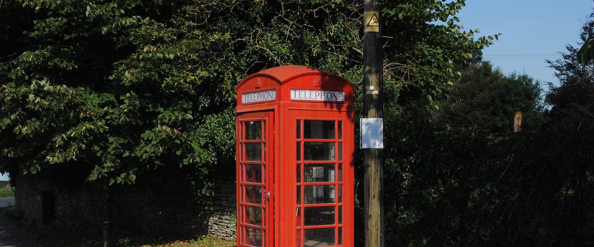 A red telephone booth on a grassy path with trees in the background.