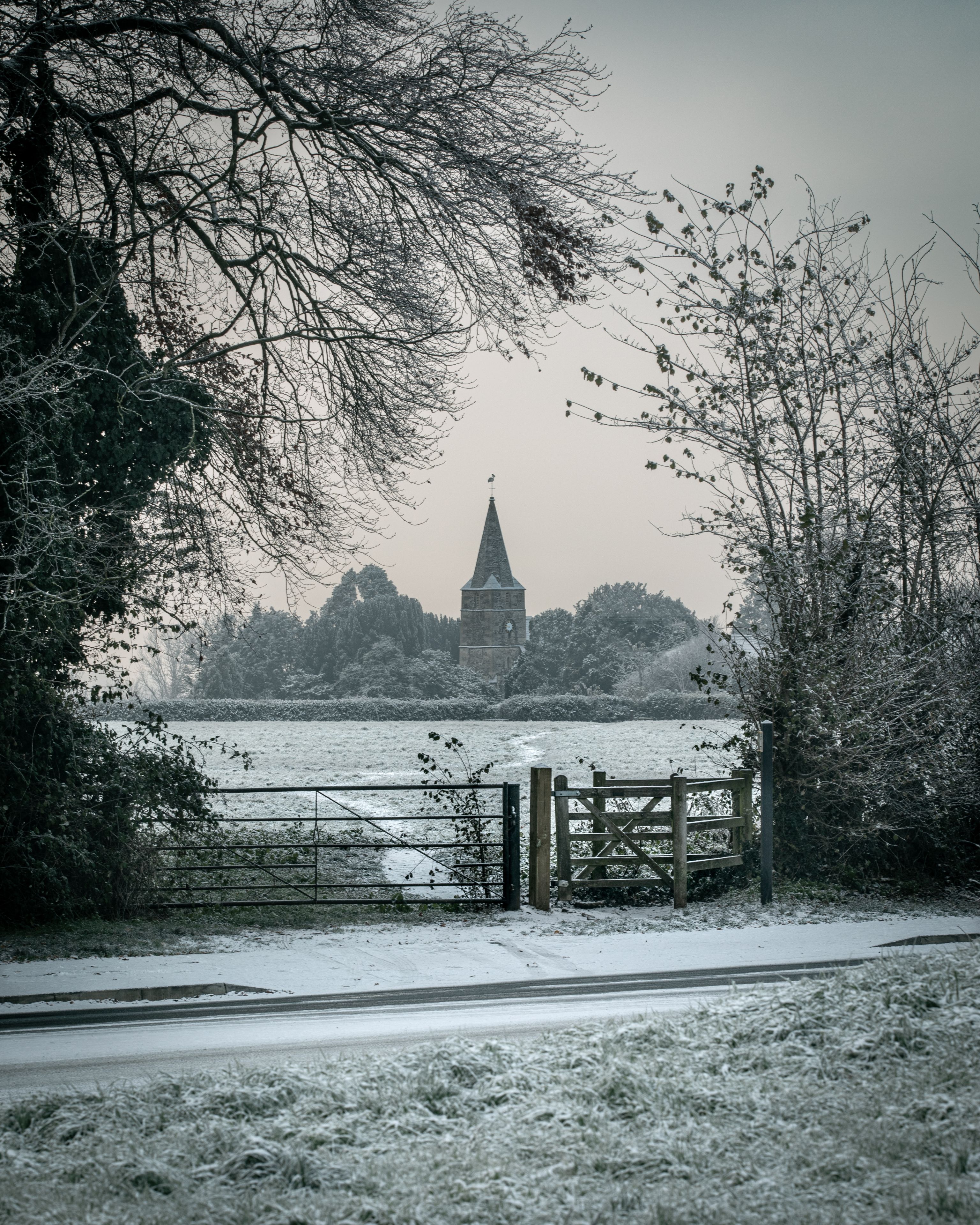 A snow-covered landscape with a church steeple, a frozen river, and a wooden fence.
