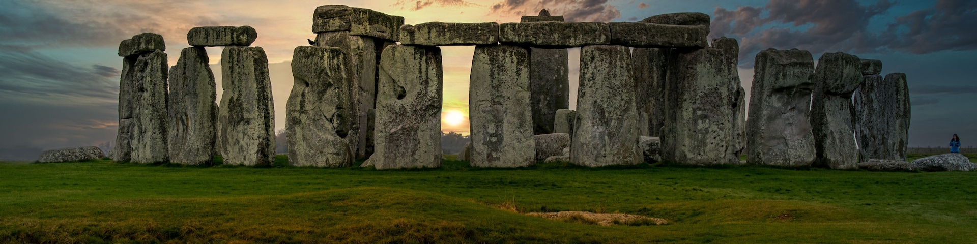Stonehenge erguido en un campo cubierto de hierba, con un atardecer al fondo.