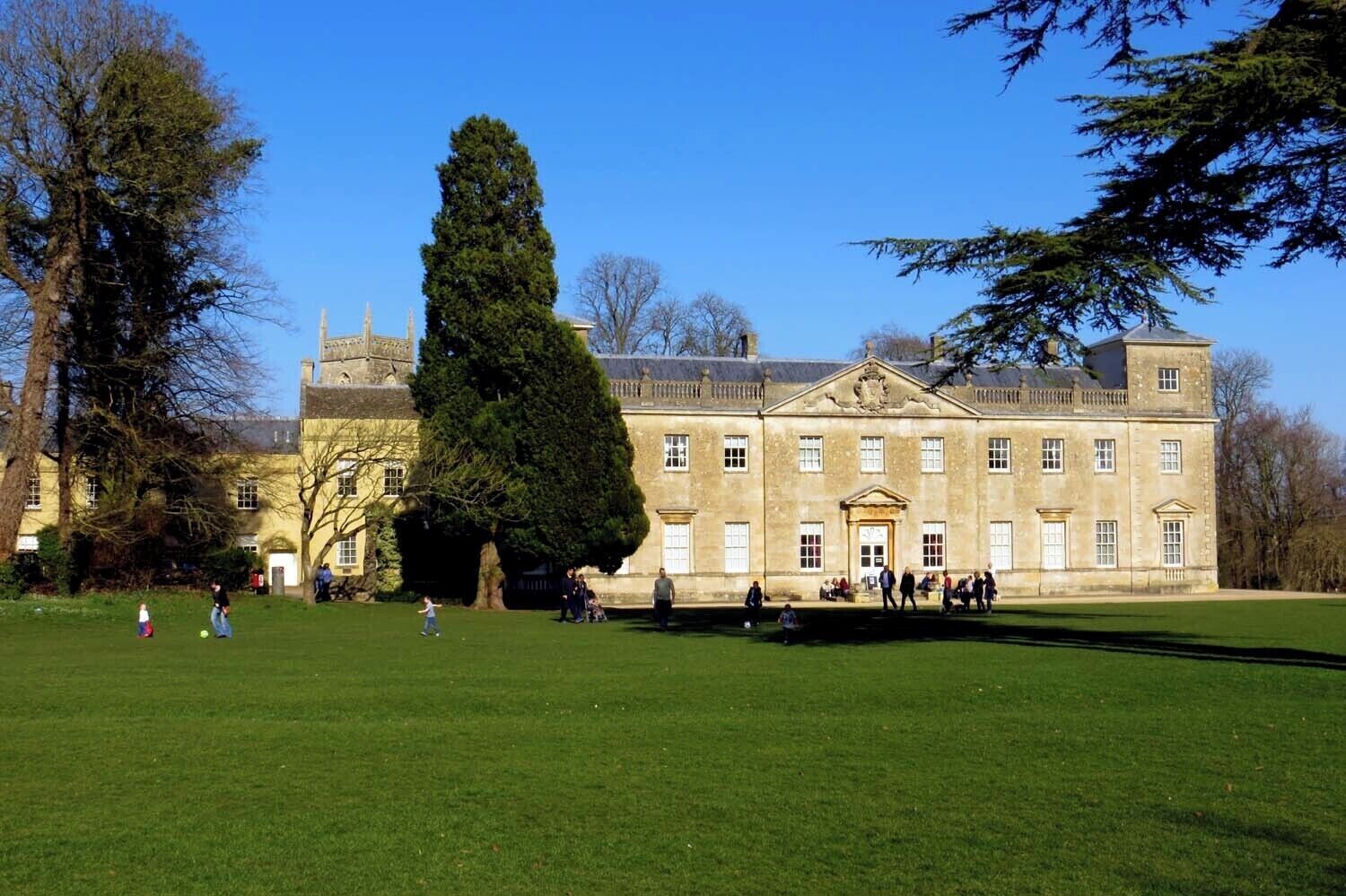 A large, historic building with a prominent central tower and symmetrical windows, surrounded by a well-maintained lawn and trees.