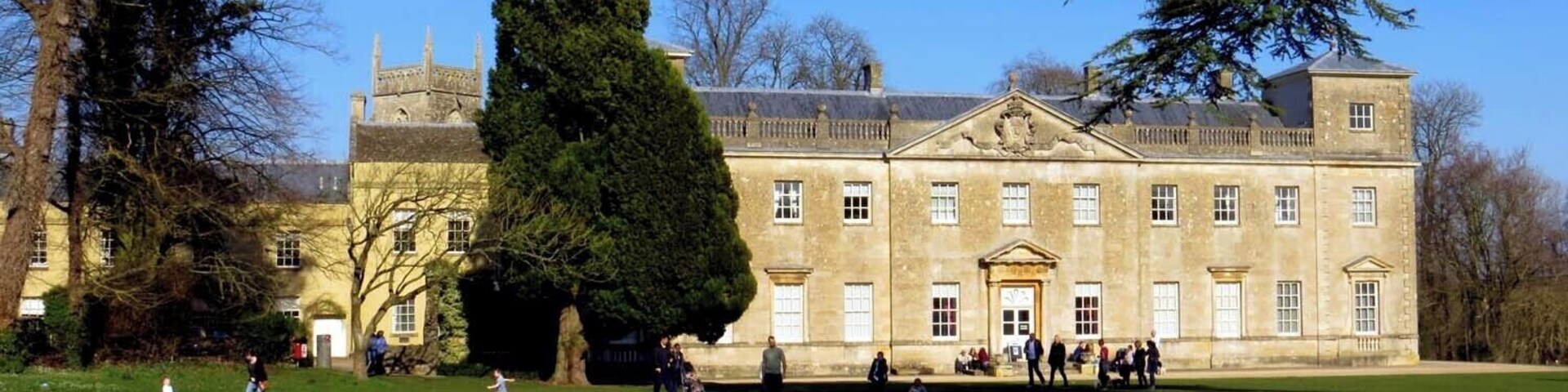 A large, historic building with a prominent central tower and symmetrical windows, surrounded by a well-maintained lawn and trees.